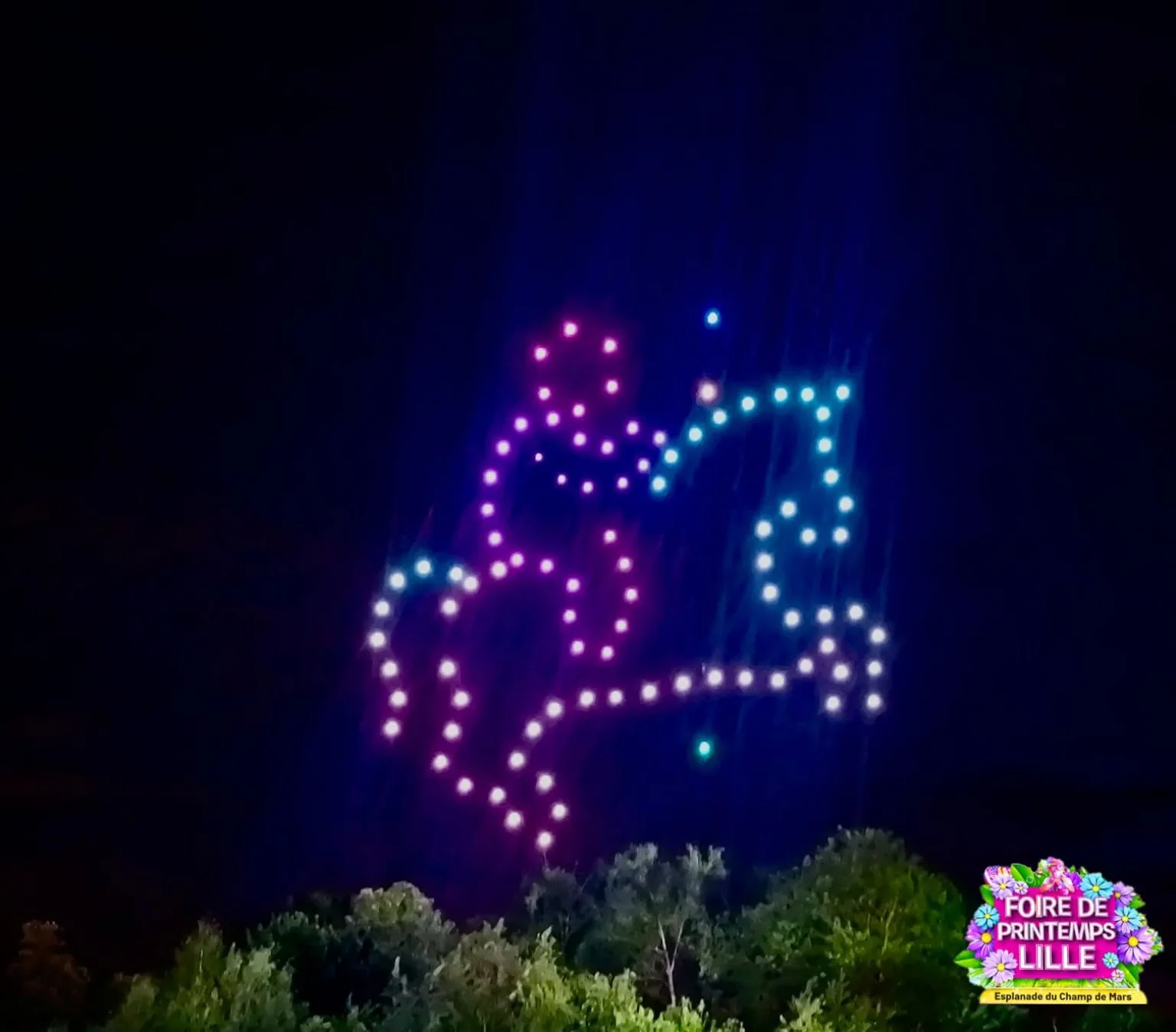 Figure aérienne lumineuse dessinée par une flotte de drones dans le ciel nocturne au-dessus d'un site événementiel